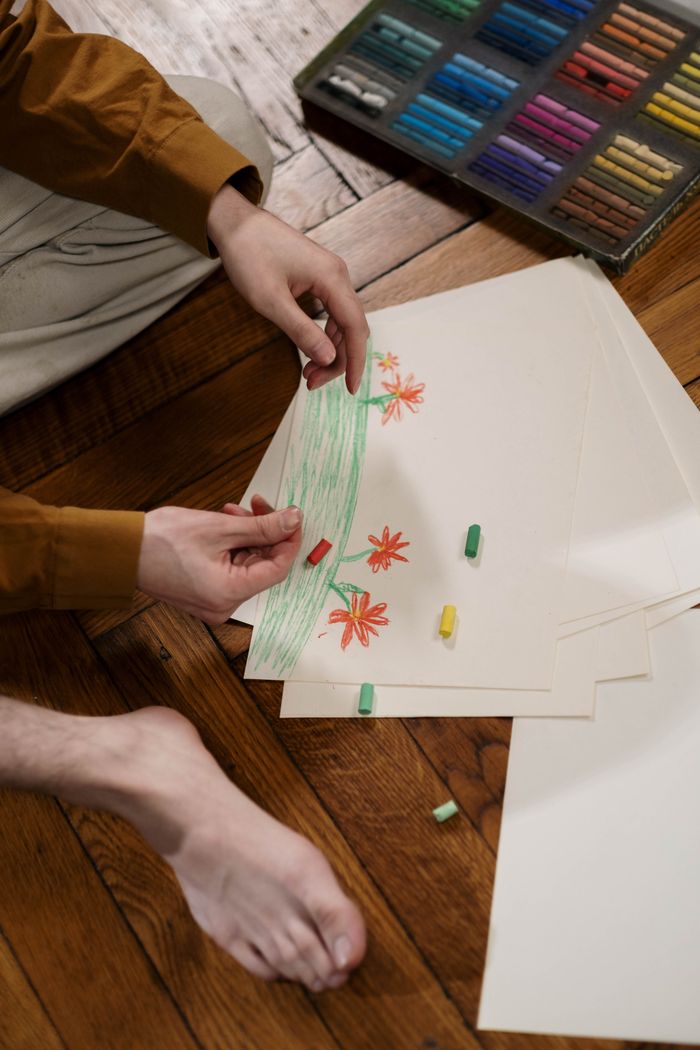 our-story Person creating artwork with oil pastels on paper indoors, showcasing creativity.