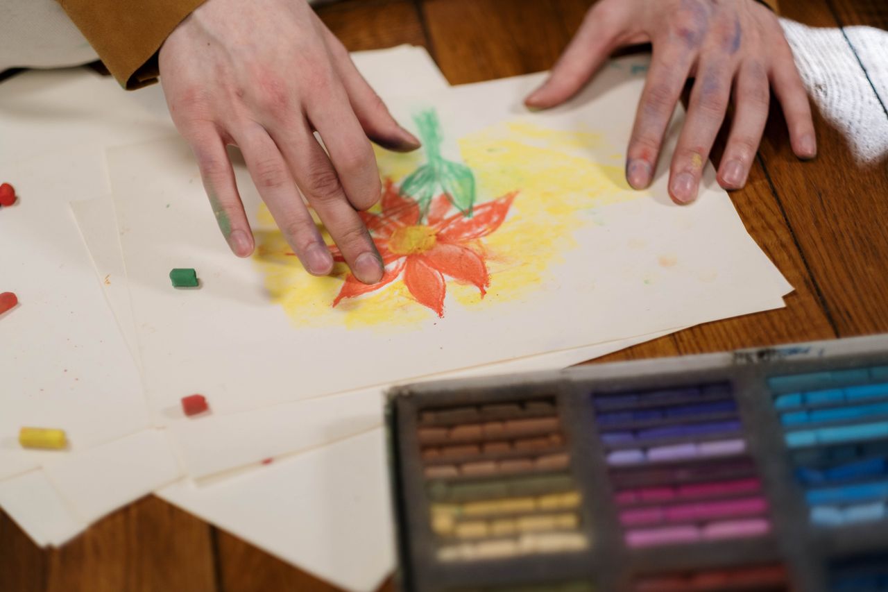 gallery-04 Hands creatively drawing a flower with pastel colors on paper, showcasing hobby art.